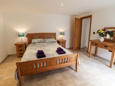 A bedroom with a wooden bed and two bedside tables with lamps and a dresser with flowers at Kingfisher in Whitby
