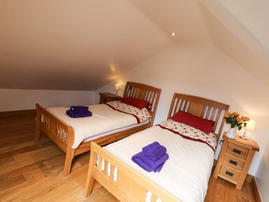 A bedroom with two single wooden beds with white bedding and purple towels on each bed at Kingfisher in Whitby