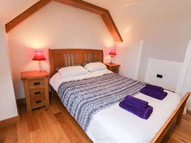 A bedroom with a wooden bed frame bedside tables with lamps and folded purple towels at Kingfisher in Whitby
