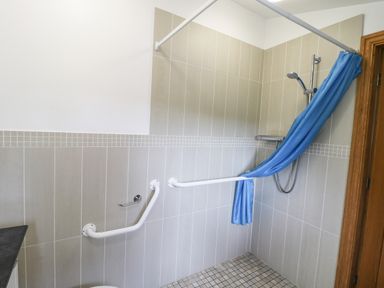A bathroom shower area with grab rails tiles and a blue shower curtain at Kingfisher Whitby