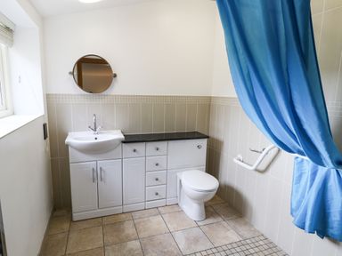 A bathroom with a white sink, toilet, round mirror, blue shower curtain, and tiled floor at Kingfisher in Whitby