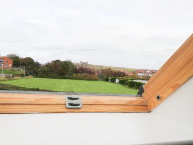 A view of a grassy field and houses beyond seen through a wooden framed skylight window at Kingfisher in Whitby