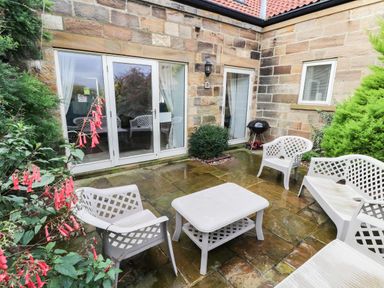 A stone patio with white outdoor chairs and a table near a barbecue grill at Kingfisher Whitby