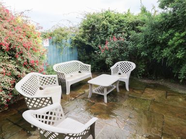 An outdoor patio with white plastic chairs and a table surrounded by green and flowering bushes at Kingfisher in Whitby