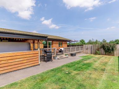 A wooden house with a patio grill and outdoor seating in a fenced garden at Kingfisher Lodge in Brandesburton