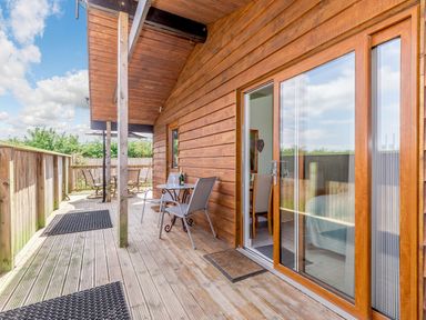 A wooden deck with outdoor chairs and tables next to sliding glass doors at Kingfisher Lodge in Brandesburton