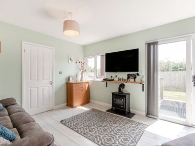 A living room with a sofa, wall-mounted television, wooden cabinet, wood stove, and sliding glass door at Kingfisher Lodge in Brandesburton