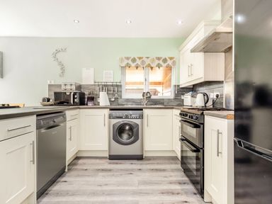 A kitchen with white cabinets appliances and a window with patterned valance at Kingfisher Lodge in Brandesburton