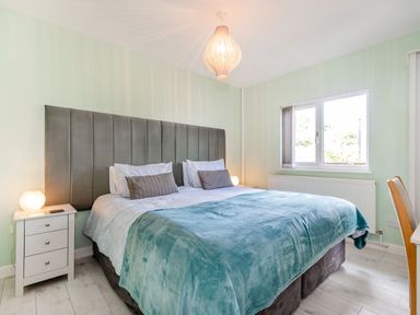 A bedroom with a large bed with gray headboard blue blanket bedside tables and a window at Kingfisher Lodge in Brandesburton