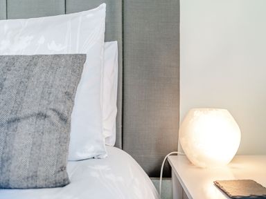 A bed with white and grey pillows next to a white bedside table with a round glowing lamp at Kingfisher Lodge Brandesburton