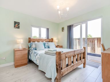 A bedroom with a wooden bed beside two wooden nightstands with lamps and sliding glass door at Kingfisher Lodge in Brandesburton