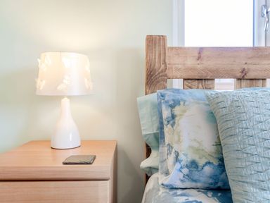 A bedside table with a butterfly patterned lamp and a wooden bed with pillows at Kingfisher Lodge Brandesburton