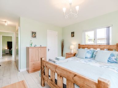 A bedroom with a wooden bed, linens, a wooden dresser, nightstand, lamp, and a window at Kingfisher Lodge in Brandesburton