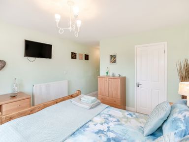 A bedroom with a wooden bed a television mounted on the wall and wooden furniture at Kingfisher Lodge in Brandesburton
