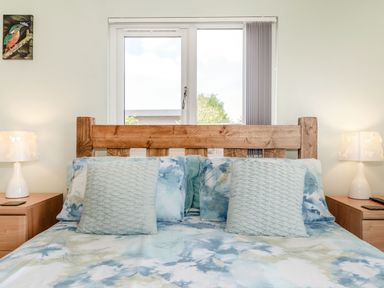 A bedroom with a wooden bed frame blue patterned bedding two bedside tables with lamps and a window behind the bed at Kingfisher Lodge in Brandesburton