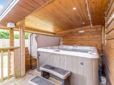 An outdoor covered wooden hot tub with steps and a partially open cover at Kingfisher Lodge in Brandesburton