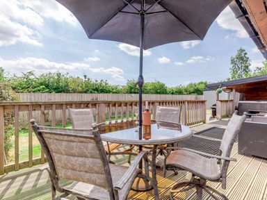 An outdoor deck with a round glass table and four chairs under a large umbrella at Kingfisher Lodge in Brandesburton