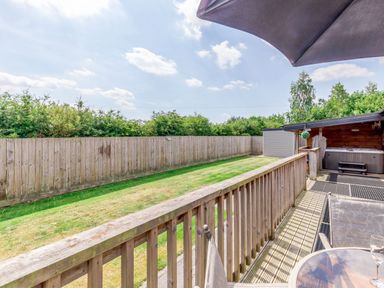 A backyard with a wooden fence a grassy lawn a covered hot tub and a patio area with outdoor furniture at Kingfisher Lodge in Brandesburton