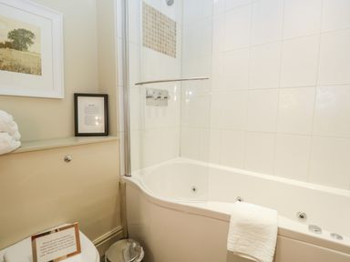 A bathroom with a bathtub shower combination a white towel on the bathtub and framed pictures on the wall at Gable End in Coniston near Hawkshead