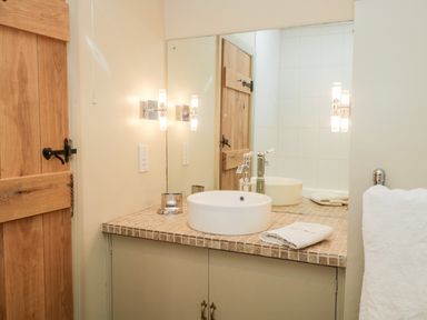A bathroom with a wooden door a round sink on a tiled countertop a large mirror and a white towel on a rack at Gable End Coniston near Hawkshead