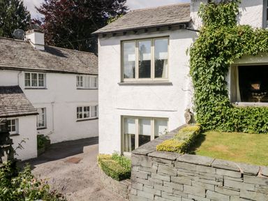 Exterior view of white painted buildings with stone roofs and a stone wall with climbing plants at Gable End Coniston near Hawkshead