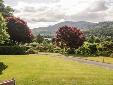 A garden with green grass and red trees overlooking hills and a lake at Gable End in Coniston near Hawkshead