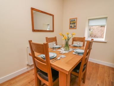 A dining room with a wooden table set for four with plates glasses and cutlery a vase with yellow flowers a mirror on the wall and a window at Y Felin - Celyn in Borth