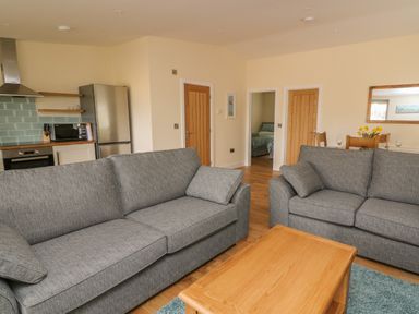 A living room with two gray sofas and a wooden coffee table next to a kitchen with a refrigerator and oven at Y Felin - Celyn in Borth
