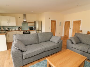 A living area with two grey sofas and a wooden coffee table adjacent to a kitchen with white cabinets and light blue tiled backsplash at Y Felin - Celyn in Borth