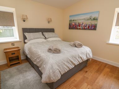 A bedroom with a bed, bedside table, two windows, a rug, and a painting of flowers at Y Felin - Celyn in Borth