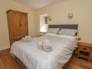 A bedroom with a bed with rolled towels on it two bedside tables and a wooden wardrobe at Y Felin - Celyn in Borth