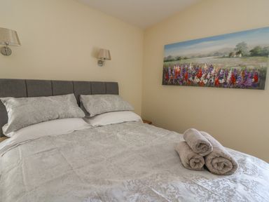 A bedroom with a bed with patterned pillows and duvet and three rolled towels on the bed with a landscape painting on the wall at Y Felin - Celyn in Borth