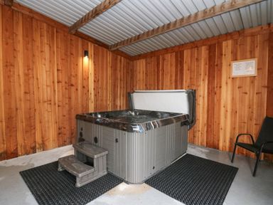 An indoor room with wooden walls a hot tub with steps and a chair at Y Felin - Celyn in Borth