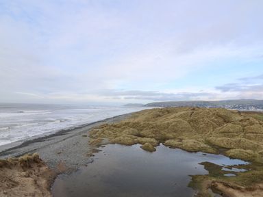 A coastal landscape with a pebble beach grassy dunes and a small pond at Y Felin - Celyn in Borth