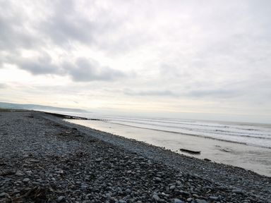 A pebble beach beside the sea with waves under a cloudy sky at Y Felin - Celyn in Borth