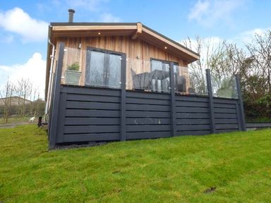 A wooden cabin with a black fenced porch and green grass in front at Crook Lodge in Allithwaite near Grange-over-Sands