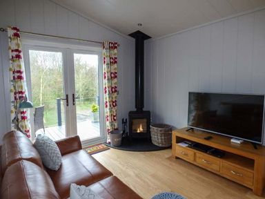 A living room with a leather sofa wood burning stove and television at Crook Lodge in Allithwaite near Grange-over-Sands