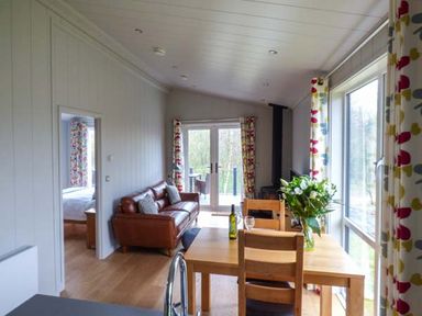 A dining table with chairs and flowers next to a sofa and glass doors in a living room at Crook Lodge in Allithwaite near Grange-over-Sands