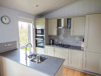 A kitchen with a sink on an island and built in appliances at Crook Lodge in Allithwaite near Grange-over-Sands