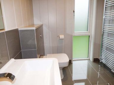 A bathroom with a sink a toilet a frosted window and a chrome towel radiator at Crook Lodge in Allithwaite near Grange over Sands
