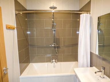 A bathroom with a bathtub shower combination a white shower curtain and a sink at Crook Lodge in Allithwaite near Grange-over-Sands