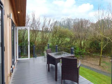 A balcony with a glass table and four chairs overlooking trees and grass at Crook Lodge in Allithwaite near Grange-over-Sands