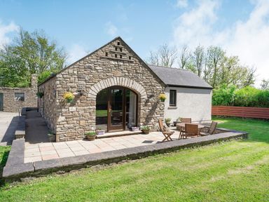 A stone and plaster cottage with patio furniture on a tiled terrace in a garden at Highbury in Spittal near Haverfordwest