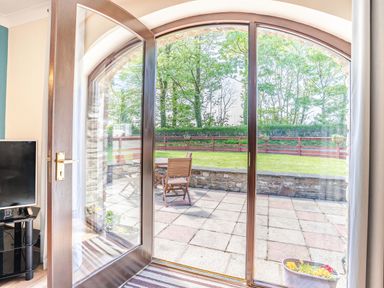 A room with a television and open wooden door leading to a patio with chairs and a lawn at Highbury in Spittal near Haverfordwest