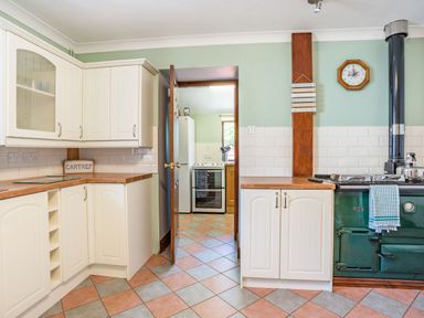 A kitchen with white cabinets wooden countertops a green stove and an open door leading to another room at Highbury in Spittal near Haverfordwest