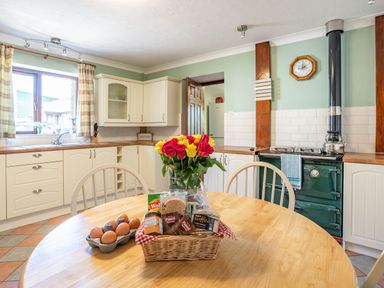 A kitchen with wooden table chairs a stove a window with curtains and cream cabinets at Highbury in Spittal near Haverfordwest
