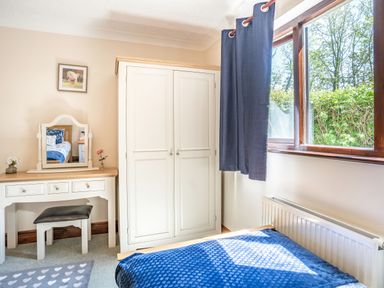 A bedroom with a white wardrobe blue curtains a dressing table and a bed near a window at Highbury in Spittal near Haverfordwest