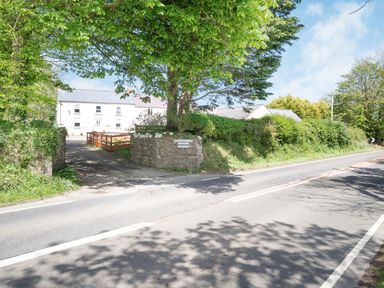 A country road with a driveway entrance to a farm and white buildings surrounded by trees at Highbury in Spittal near Haverfordwest