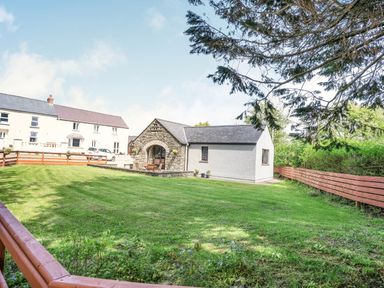A fenced grassy yard with a small stone and white building and houses in the background at Highbury in Spittal near Haverfordwest