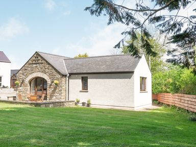 A small building with a stone arch entrance and wooden chairs on a grass lawn at Highbury in Spittal near Haverfordwest